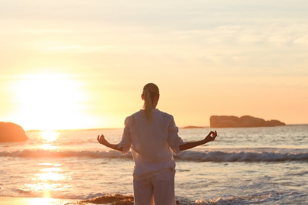 Übendes Yoga der Frau während des Sonnenuntergangs