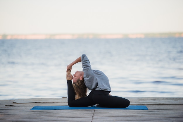 Übendes Yoga der jungen Sportfrau auf dem Strand