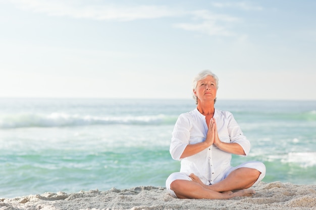 Übendes Yoga der reifen Frau auf dem Strand