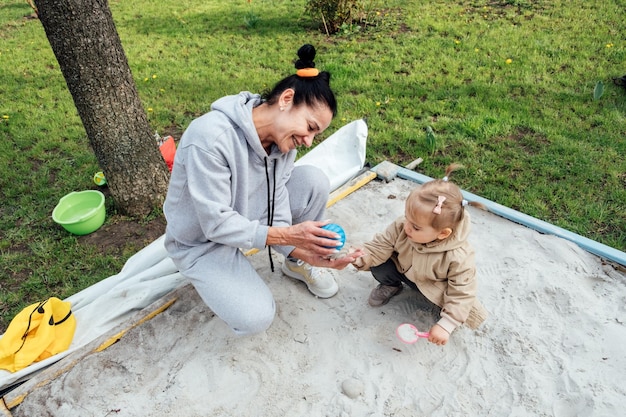 Beneficios de Sand Play Sandpit ideas de juego para que los niños aprendan mientras se divierten Abuela anciana y nieta pequeña jugando juntos en la caja de arena en el jardín de primavera