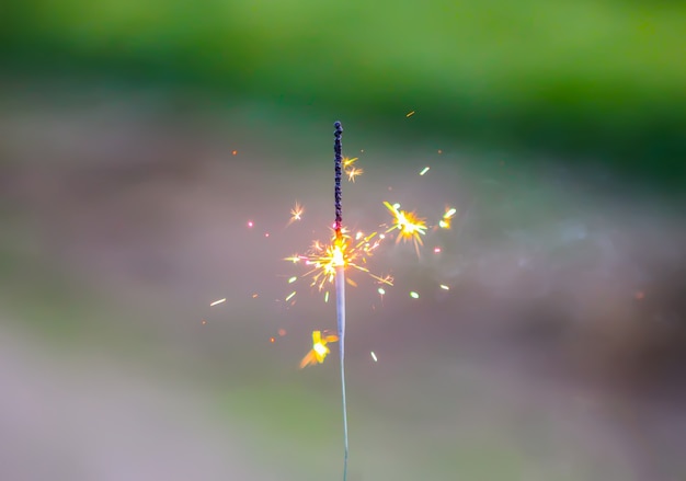 Una bengala ardiente sobre fondo de hierba verde. Detalle festivo de la fiesta de verano.