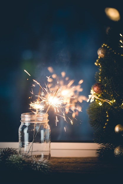 Bengala de fiesta de navidad o año nuevo en un frasco frente a la ventana en la decoración de navidad de fondo oscuro