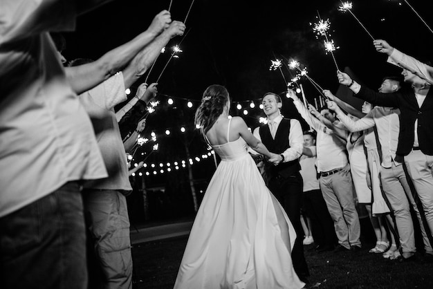 Foto bengalas en la boda de los recién casados en manos de alegres invitados.