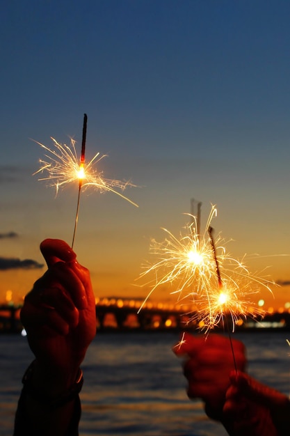 Bengalas en el fondo del cielo nocturno manos de amigos durante la celebración