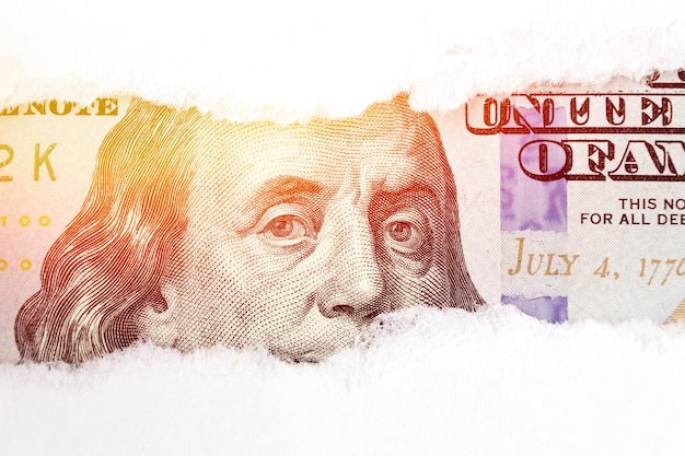 Benjamin Franklin Porträt auf 100 Banknote in zerrissenem Papierloch mit Sonnenlicht Dolar USA Nahaufnahme Spareinlagen und der US-Dollar