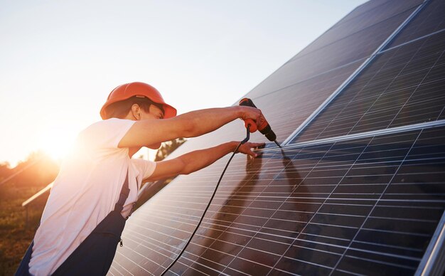 Benutzung eines drahtlosen Schraubenziehers Mann in blauer Uniform im Freien mit Solarbatterien an einem sonnigen Tag