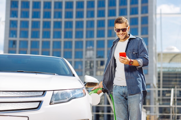 Benzin. Selbstbewusster positiver Mann, der sein Auto tankt, während er an der Tankstelle ist