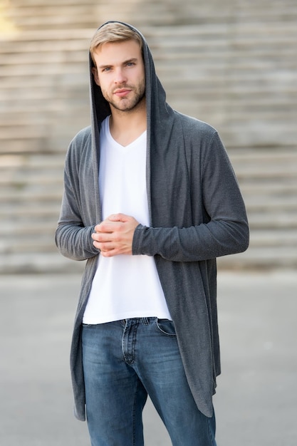Bequeme kleidung für den täglichen gebrauch toller geschmack, um sich gut zu kleiden männlicher modeeinfluss modischer junger modellmann streetstyle-outfit schöner mann mit kapuze im städtischen hintergrund modetrend