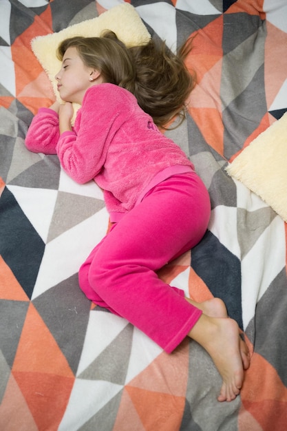 Bequemer Schlafanzug zum Entspannen. Kleines Kind des Mädchens trägt weiche, süße Pyjamas, während es sich auf dem Bett entspannt. Müdes Baby, das sich entspannt. Pyjamas und Kleidung für zu Hause. Pyjamas und Schlafzimmertextilien. Kinder genießen Freizeit.