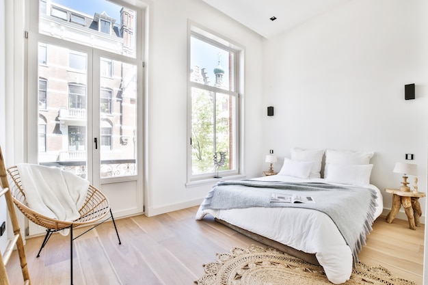 Bequemes Bett mit Decke und Kissen in der Nähe von Lampen und Stuhl im geräumigen Schlafzimmer in moderner Wohnung