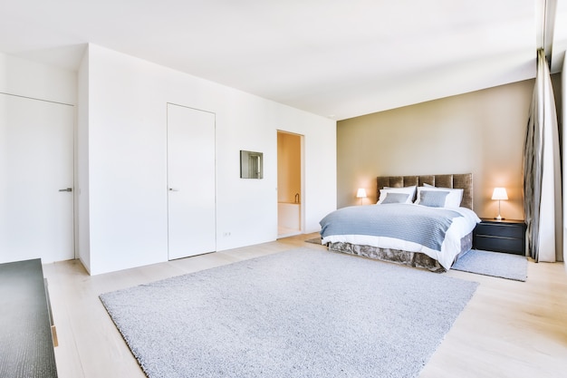 Bequemes Bett und weicher Teppich im geräumigen Schlafzimmer mit minimalistischem Interieur