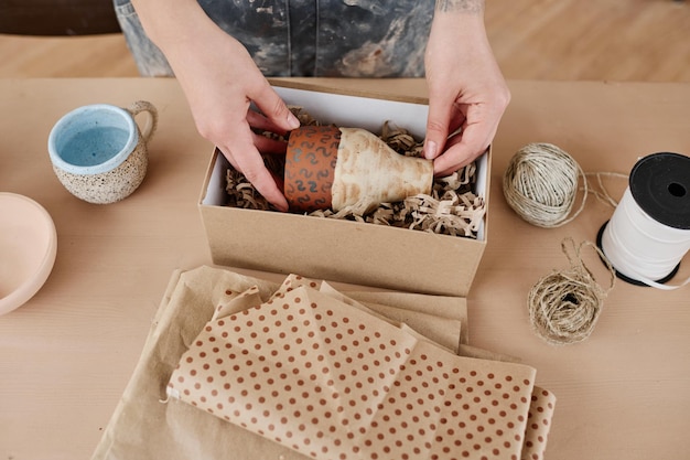 Über dem Winkel der Hände der Handwerkerin, die handgefertigten Krug oder Vase in die Kiste legt