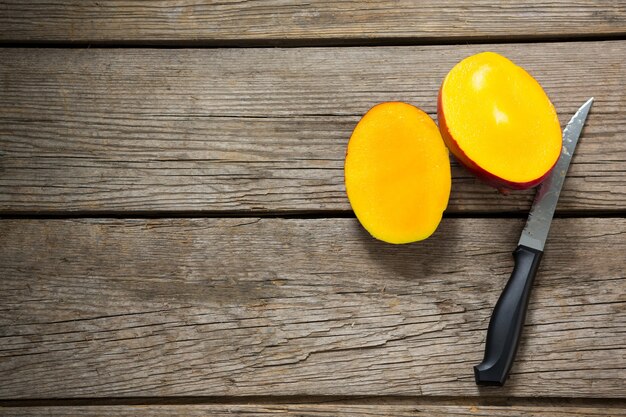 Über halbierter Mango und Messer auf Holztisch