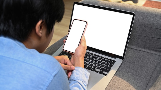 Über Schulteransicht des Mannes, der auf Sofa ruht, das mit Laptop-Computer arbeitet und Handy verwendet