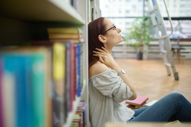 Überarbeiteter Forscher sitzt auf dem Boden in der Bibliothek