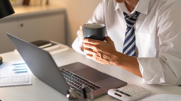 Überarbeitungskonzept Ein Büromann, der spät arbeitet und dabei eine Tasse Kaffee trinkt, während er sich konzentriert