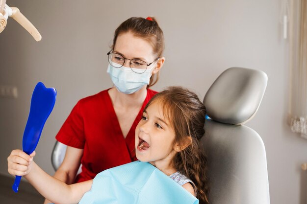 Beratung mit Kinderzahnarzt in der Zahnheilkunde Zahnbehandlung Kind, das den Zahnarzt im Spiegel betrachtet Glücklicher Kindpatient der Zahnheilkunde