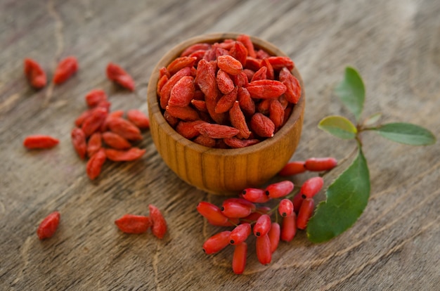 Berberries perto da pilha de goji berries e tigela de madeira com goji em madeira