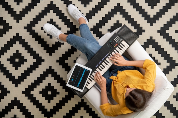 Überblick über junge Frauen in Freizeitkleidung, die auf einem weißen Ledersessel im Wohnzimmer sitzen und die Synthesizer-Tastatur verwenden, während sie Musik aufnehmen