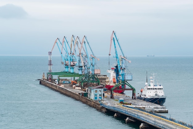 Berço de carga com guindastes portuários e navios atracados contra o pano de fundo do mar aberto