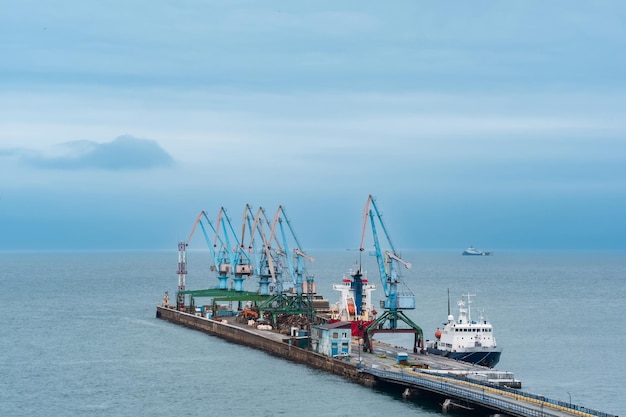 Berço de carga com guindastes portuários e navios atracados contra o pano de fundo do mar aberto