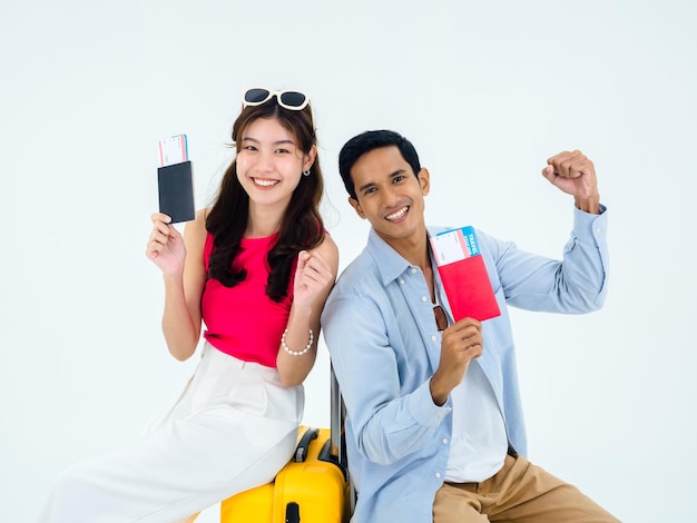 Bereit, frohen Urlaub Sommerurlaub Konzept zu reisen Lächelndes asiatisches Paar, das die erhobene Faust mit dem Pass mit Erfolg hält Junge Frau und Mann sitzen auf dem Koffer, der auf weißem Hintergrund isoliert ist