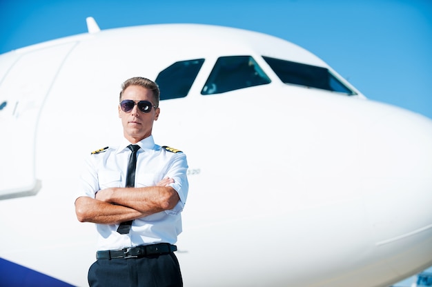 Bereit für den Himmel. Selbstbewusster männlicher Pilot in Uniform mit verschränkten Armen