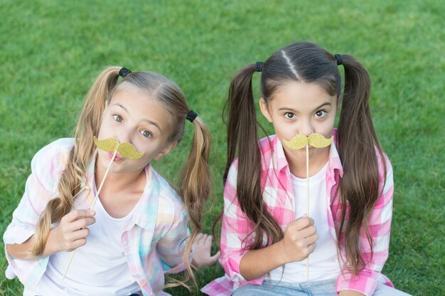 Bereit für die Party. Kleine Kinder halten Schnurrbartstützen grünes Gras. Kleine Mädchen mit Photobooth-Requisiten auf Stöcken. Party-Requisiten und Zubehör. Perfekte Requisiten zum Feiern. Sommerferien.