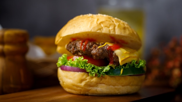 Bereit, hausgemachten Fleisch-Hamburger mit einem Glas Getränkeunschärfe im Hintergrund zu essen.