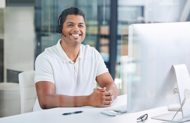 Bereit, Ihnen zu helfen Aufnahme eines hübschen jungen Geschäftsmanns, der allein in seinem Büro sitzt und ein Headset trägt, während er seinen Computer benutzt