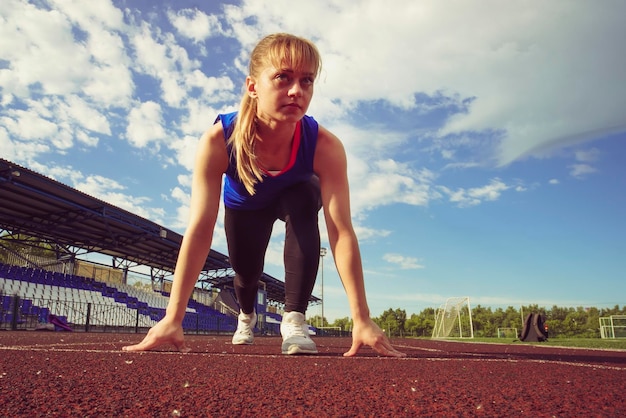 Bereit zu gehen Sportlerin an der Startlinie einer Stadionstrecke, die sich auf eine Rücklaufansicht vorbereitet Fitness-Mädchen bereitet sich darauf vor, von einem niedrigen Startpunkt aus zu laufen Gesunder Lebensstil