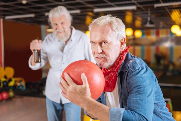 Bereit zu streiken. Netter alter Mann, der eine Bowlingkugel hält, während er sich darauf vorbereitet, einen Schlag zu schlagen