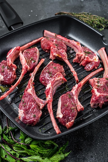 Bereit zum Kochen Rohes Lamm, Hammel hackt Steaks in einer Pfanne mit Kräutern. Schwarzer Hintergrund. Ansicht von oben.