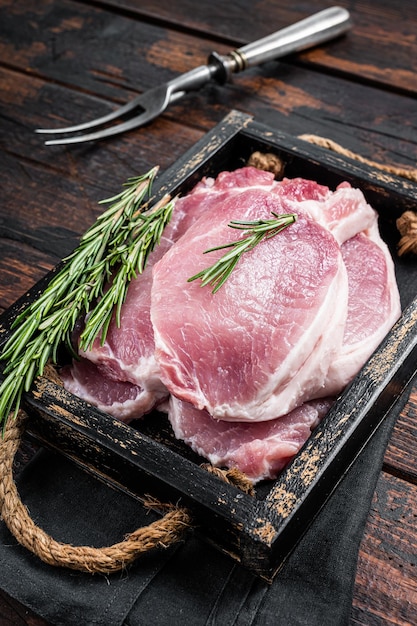 Bereit zum Kochen von rohen Schweinekotelettsteaks in einem Holztablett mit Rosmarin Holzhintergrund Draufsicht