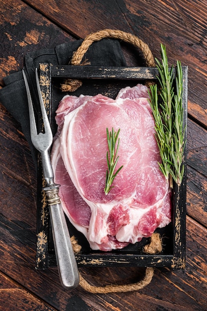 Bereit zum Kochen von rohen Schweinekotelettsteaks in einem Holztablett mit Rosmarin Holzhintergrund Draufsicht