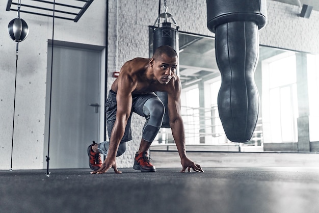 Bereit zum Start. Nackter Oberkörper junger afrikanischer Mann Position für ein Rennen beim Training im Fitnessstudio