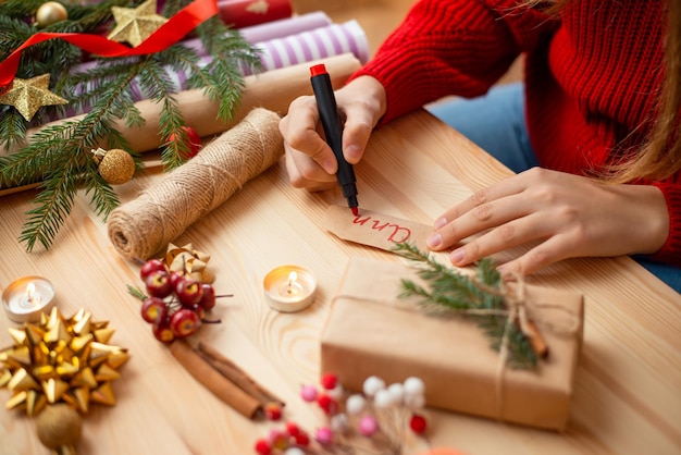 Bereiten Sie Geschenke für Weihnachten vor Hände eines jungen Mädchens, das den Namen des Empfängers des Freundes schreibt, um ihn der Schachtel hinzuzufügen