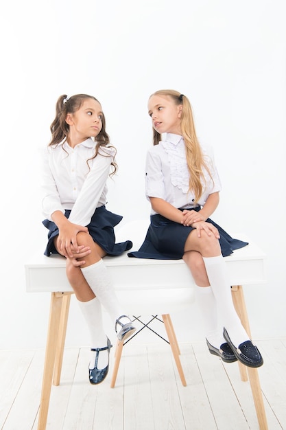 Bereiten Sie sich auf den Schulanfang vor. Grundschüler in formeller Uniform sitzen auf dem Tisch. Kleine Schulmädchen, die im Schulklassenzimmer sprechen Kleine Kinder genießen die Schulpause.