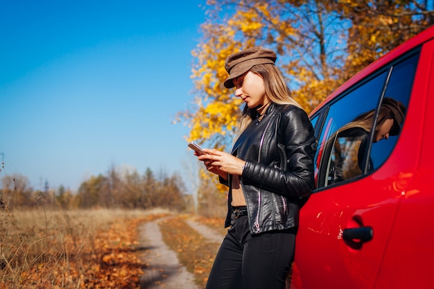 Bereitstehendes Auto der jungen Frau unter Verwendung des Smartphone auf Herbststraße. Der Fahrer hielt automatisch an, um ein besseres Signal zu erhalten