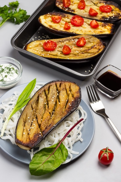 Berenjena al horno con verduras y fideos de arroz en un plato. Berenjena al horno con tomate en palet. Salsa en un tazón de vidrio. Vista superior