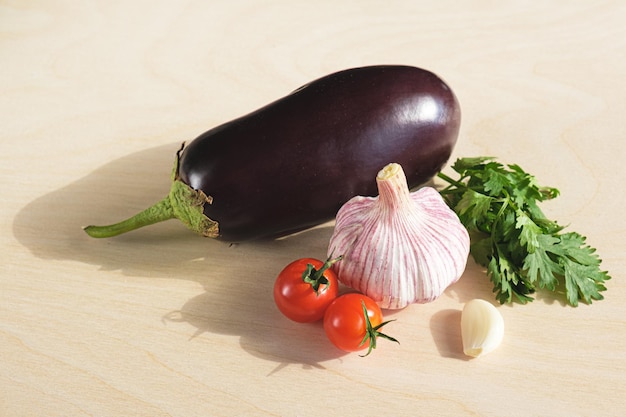 Berenjena fresca una cabeza de rama de ajo de tomates cherry y una ramita de cilantro fresco sobre tabla de madera