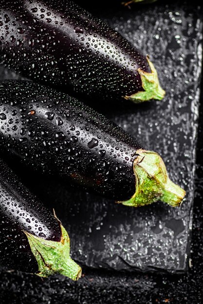 Berenjena madura fresca con gotas de agua en un tablero de piedra