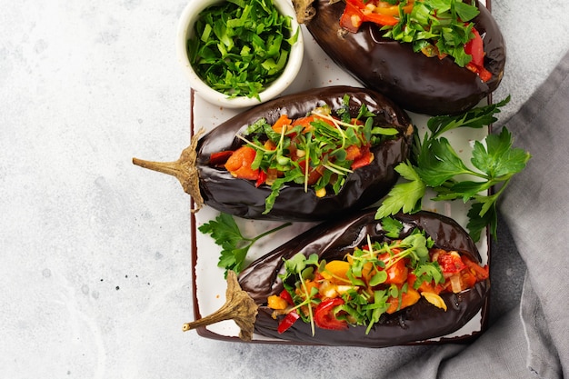 Berenjena rellena al horno con diferentes verduras, tomate, pimiento, cebolla y perejil en piedra gris o mesa de hormigón