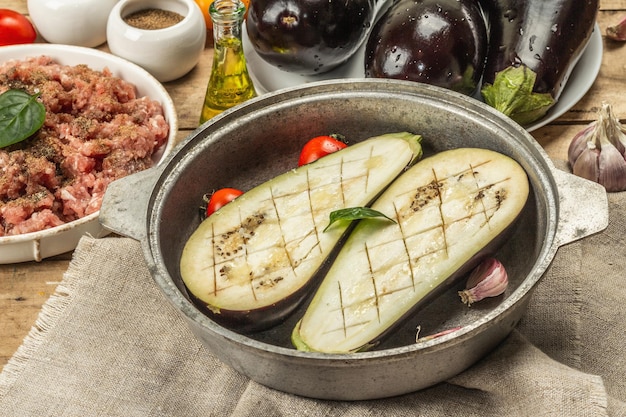 Berenjena rellena lista para hornear con carne molida, verduras y especias. Fondo de madera, utensilio de cocina, estilo rústico, cerrar