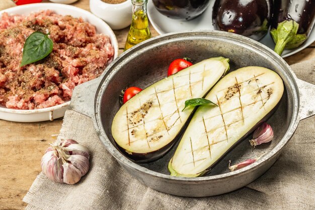 Berenjena rellena lista para hornear con carne molida, verduras y especias. Fondo de madera, utensilio de cocina, estilo rústico, cerrar