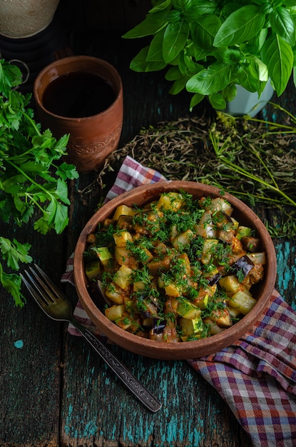 Berenjenas asadas con verduras y patatas en un plato de barro (ketsa). Comida sana casera de estilo rústico.