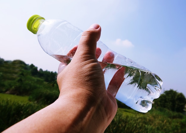 Übergeben Sie das Halten der Plastikwasserflasche auf unscharfem grünem Gartenhintergrund