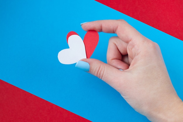 Übergeben Sie das Halten eines roten und weißen Herzens auf einem roten und blauen Hintergrund. Hintergrund für den Valentinstag