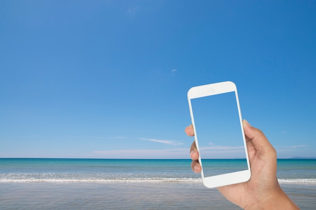 Übergeben Sie das Halten von Smartphone mit tropischem Meer und Strand als Hintergrund