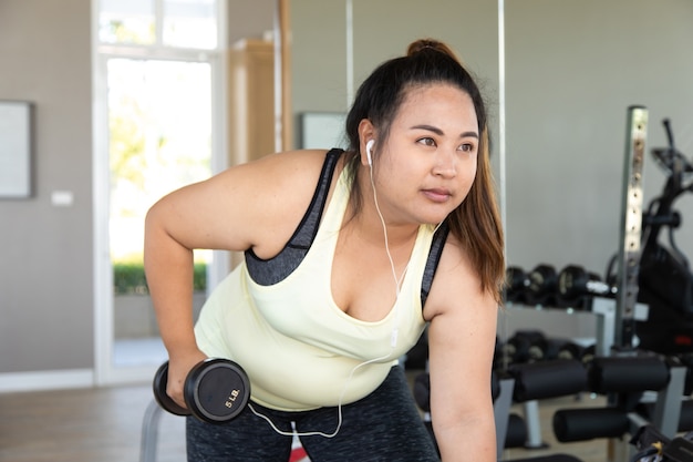 Übergewichtige Frau, die ein Fitness-Training mit Gewichten im Fitnessstudio macht. Gesunder Lebensstil und Sportkonzepte.